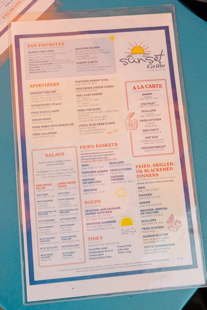 Seafood restaurant menu featuring sunset grill logo, fan favorites, appetizers, salads, soups, sides, fried baskets, and dinner options with prices.