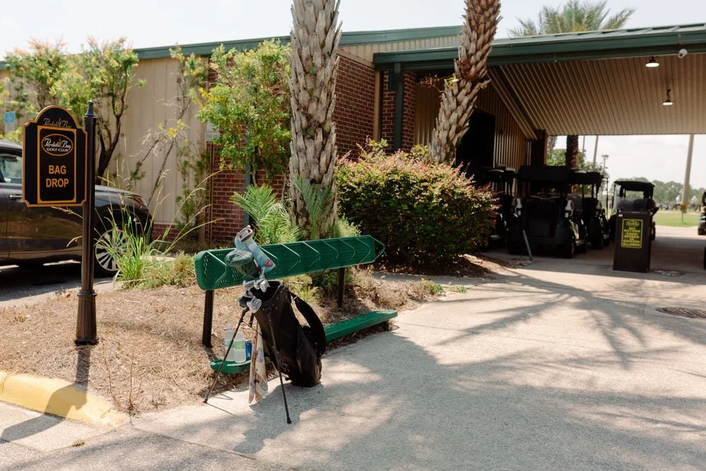 Golf course bag drop area with golf clubs, bags, and golf carts visible in the background.