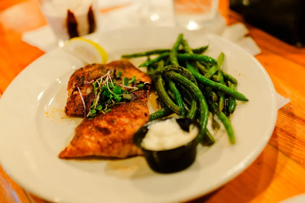 Plate with grilled fish, green beans, lemon wedge, and a side of dipping sauce.