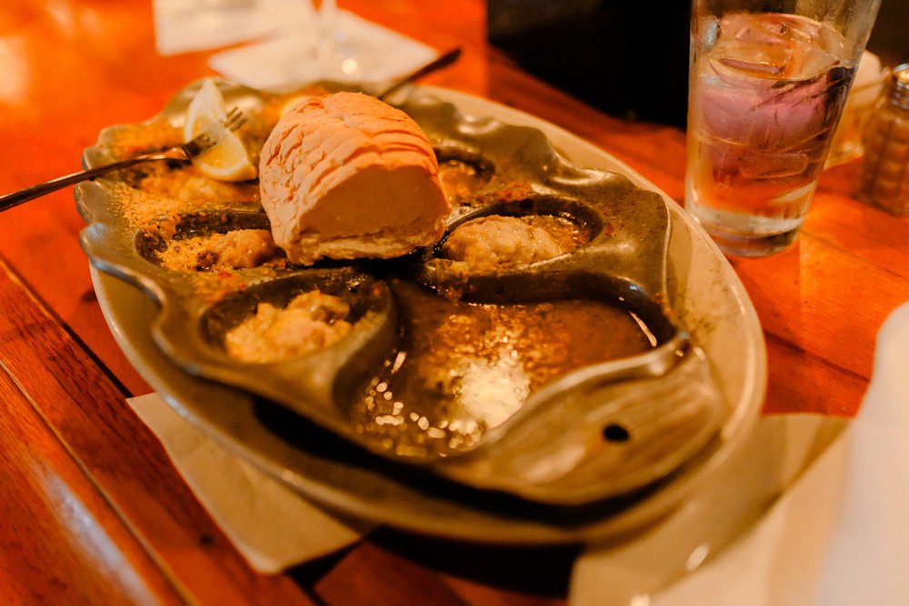Seafood dish with mussels and a scoop of melted butter on a decorative ceramic plate, on a wooden table, with a glass of water nearby.