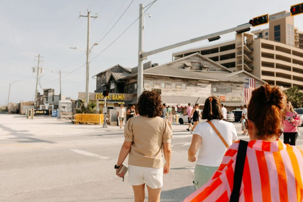 People crossing a street near a weathered building with a yellow sign that reads 'FIGURE BAMA,' in an urban area with utility poles and modern buildings in the background.