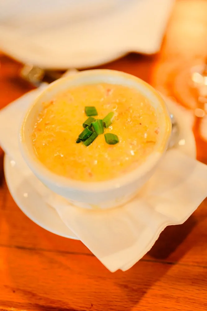 A cup of creamy, yellow soup garnished with chopped green onions, served on a white napkin and placed on a wooden table.