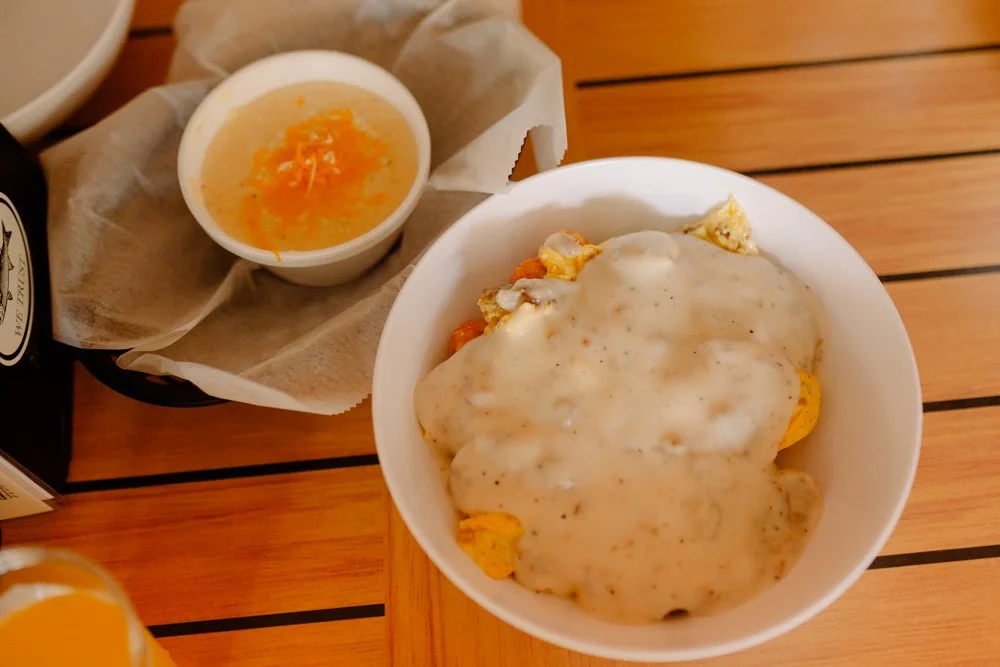 Bowl of chicken pot pie topped with gravy, small container of orange sauce or marmalade, and a black bottle on a wooden table.