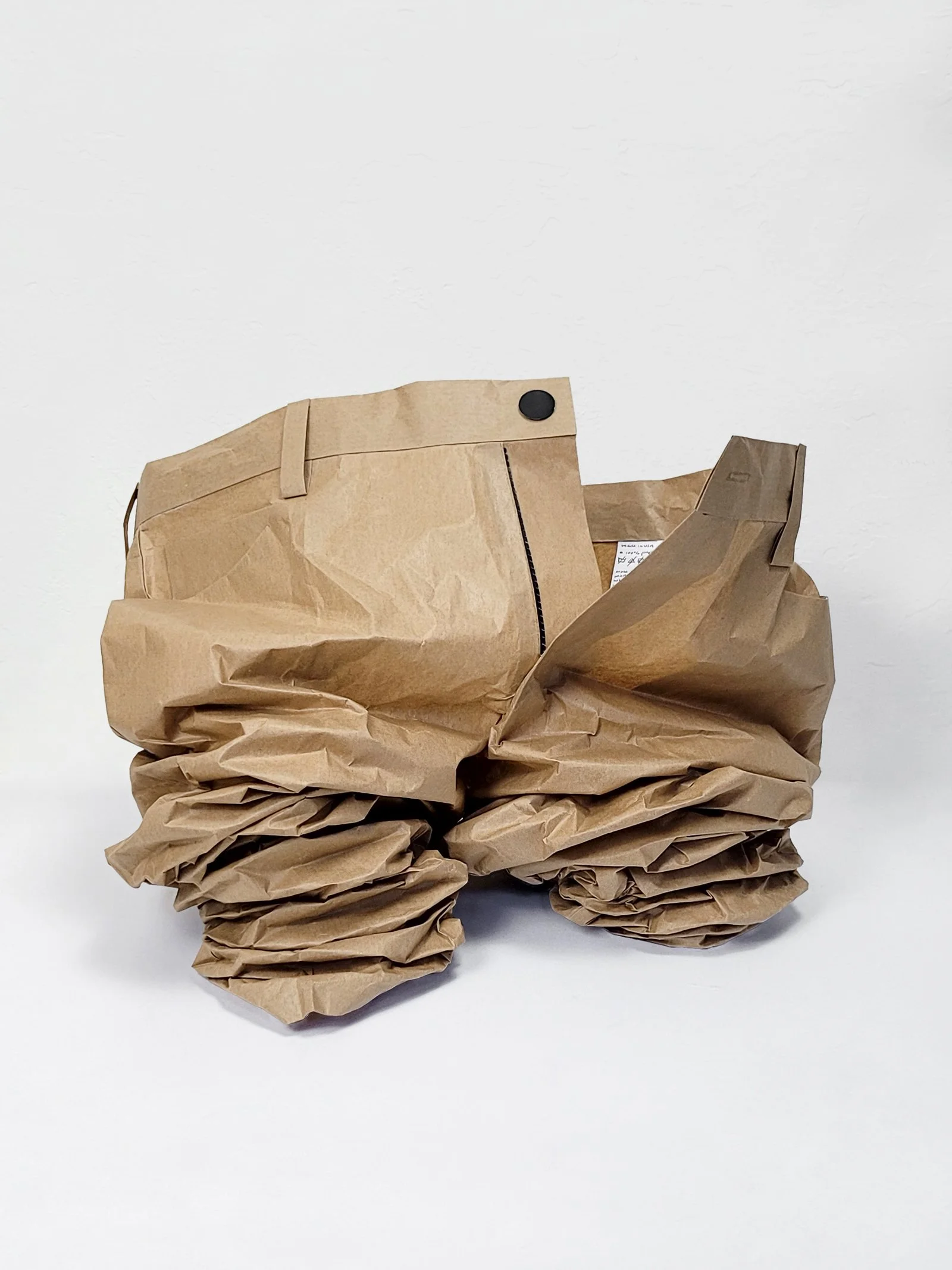 Crumbled up khaki pants made out of kraft paper on neutral background