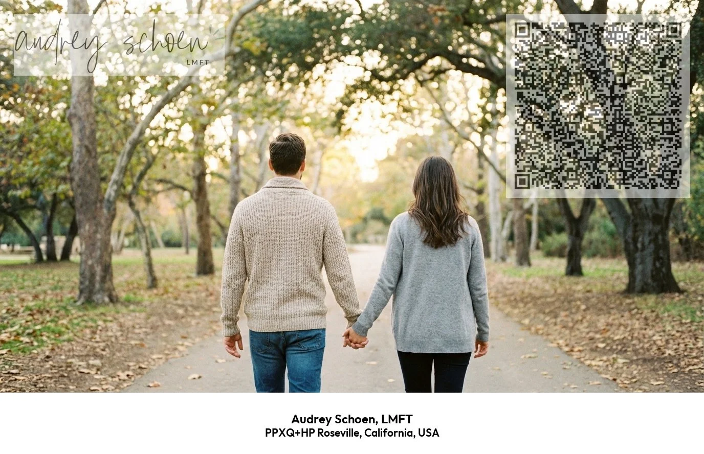 A man and woman walk hand in hand down a tree-lined path in a park during autumn, with fallen leaves on the ground and sunlight filtering through the trees.