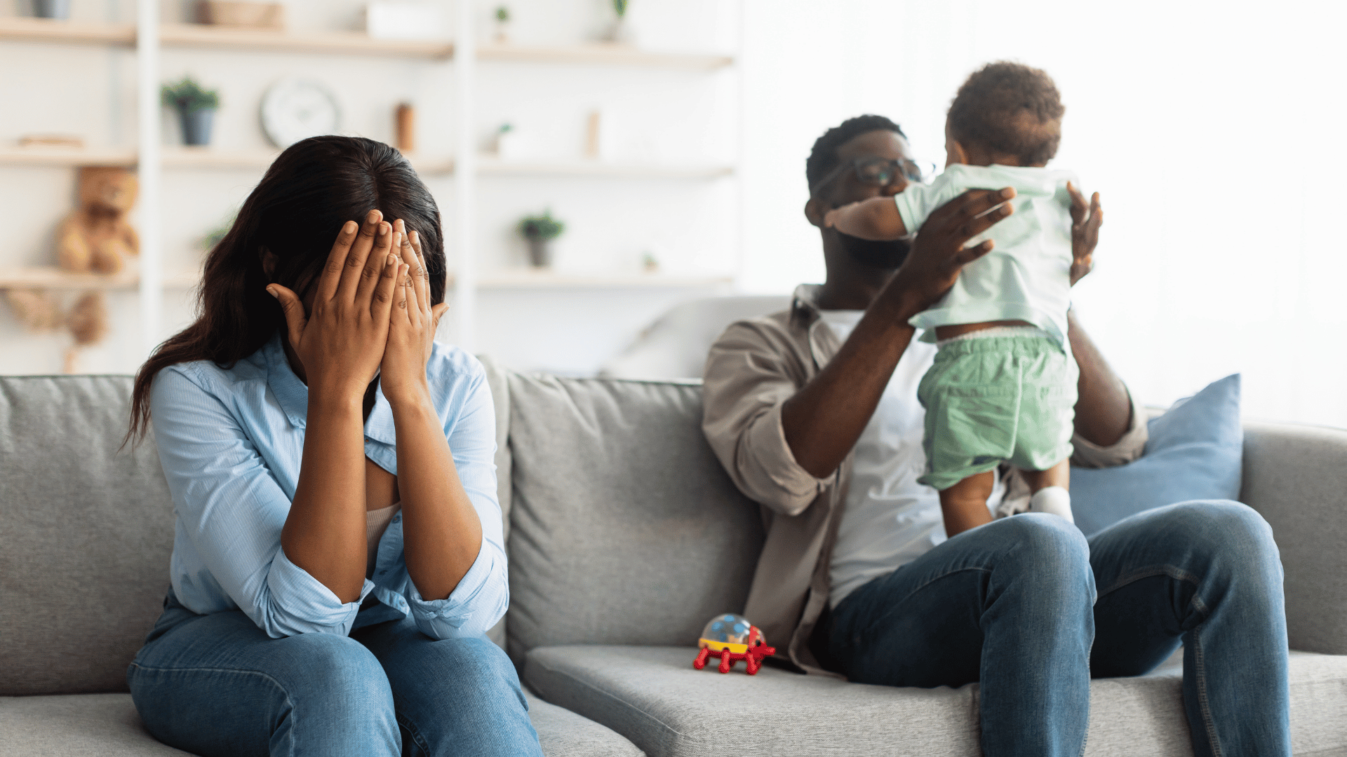 Exhausted mom sitting on couch while energetic dad plays with happy child beside her – parenting burnout and family dynamics
