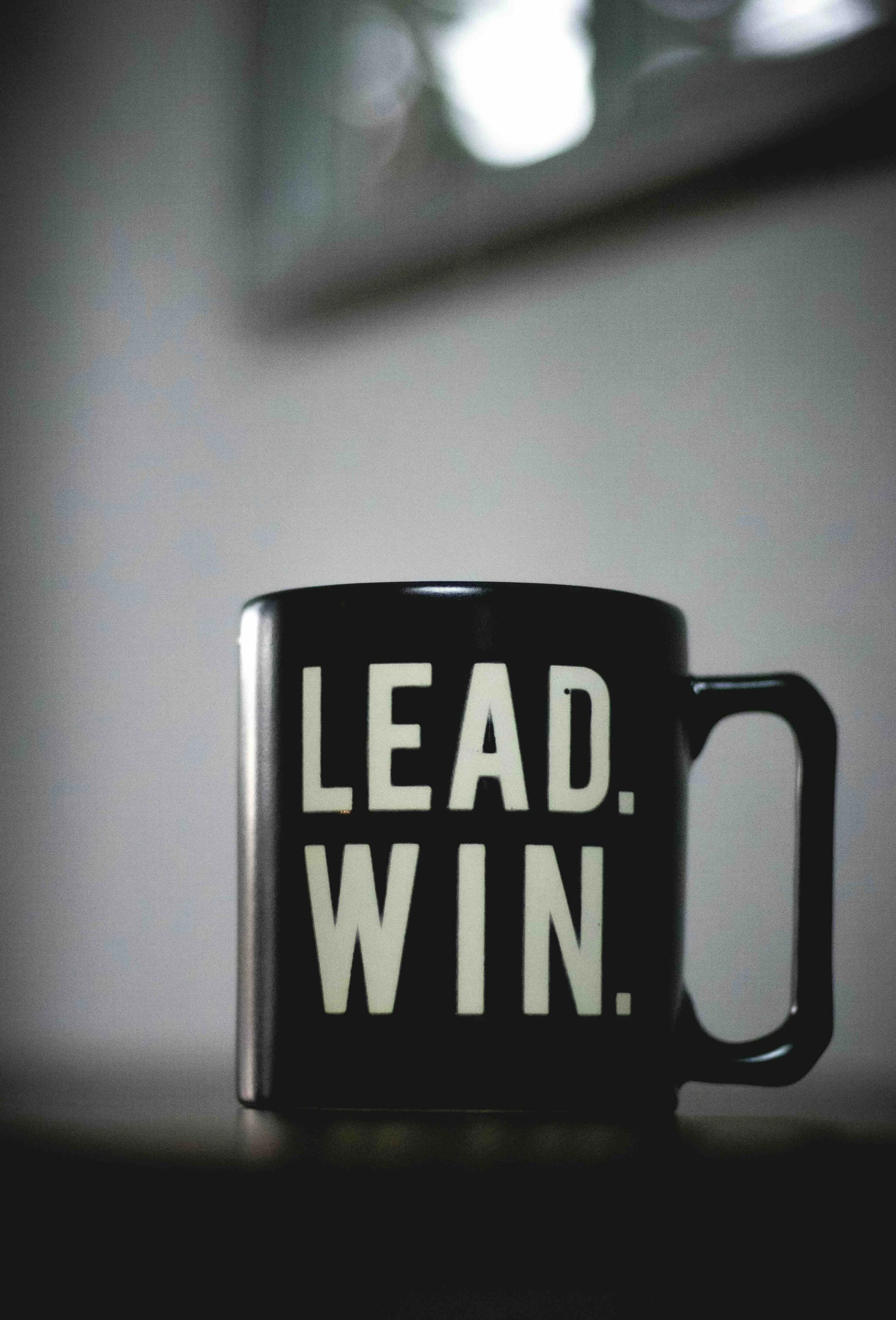 Close-up of a black coffee mug with the words 'LEAD. WIN.' written in bold white letters, with light reflections on the mug's surface.