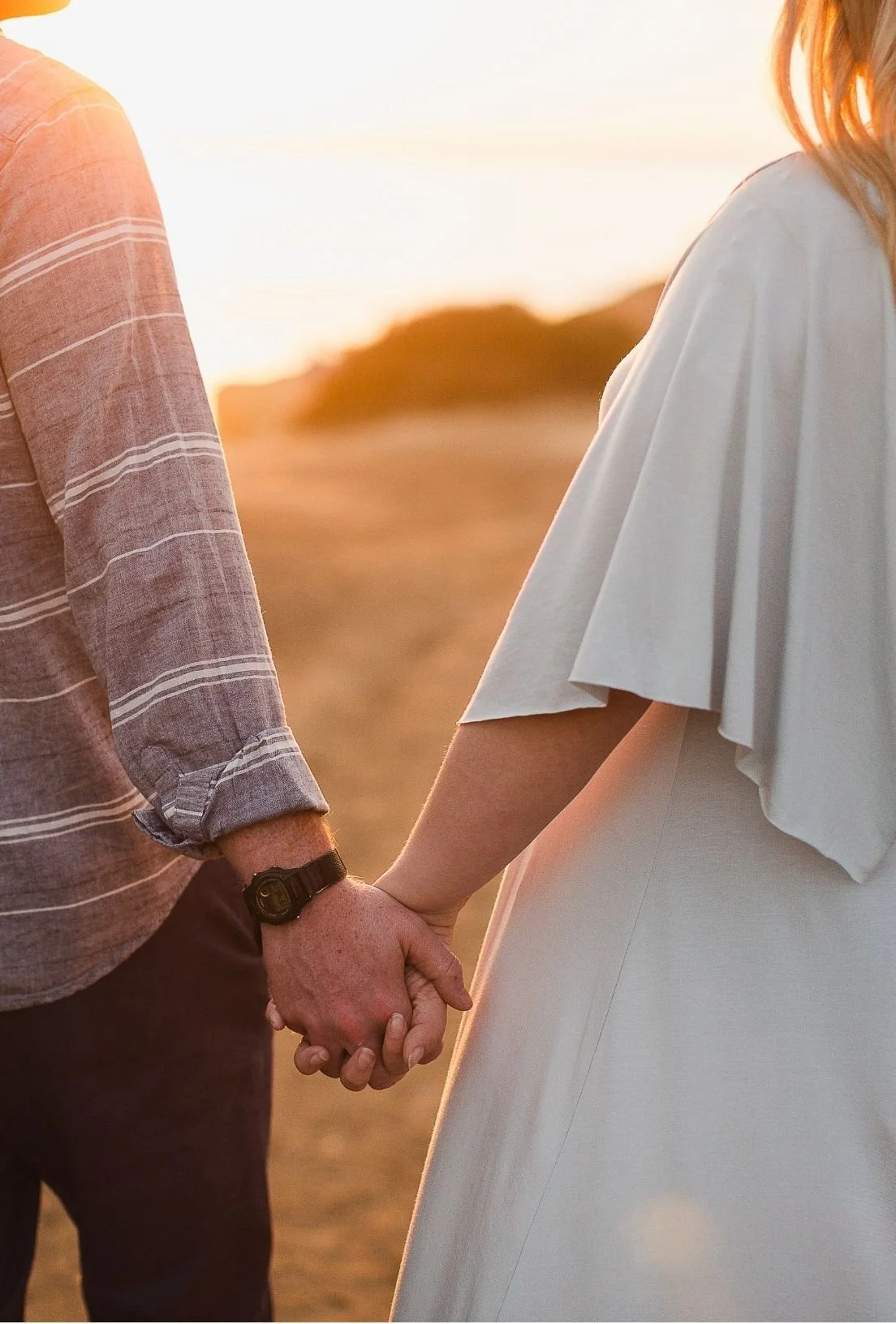 A couple holding hands outdoors during sunset, with a blurred natural landscape in the background.