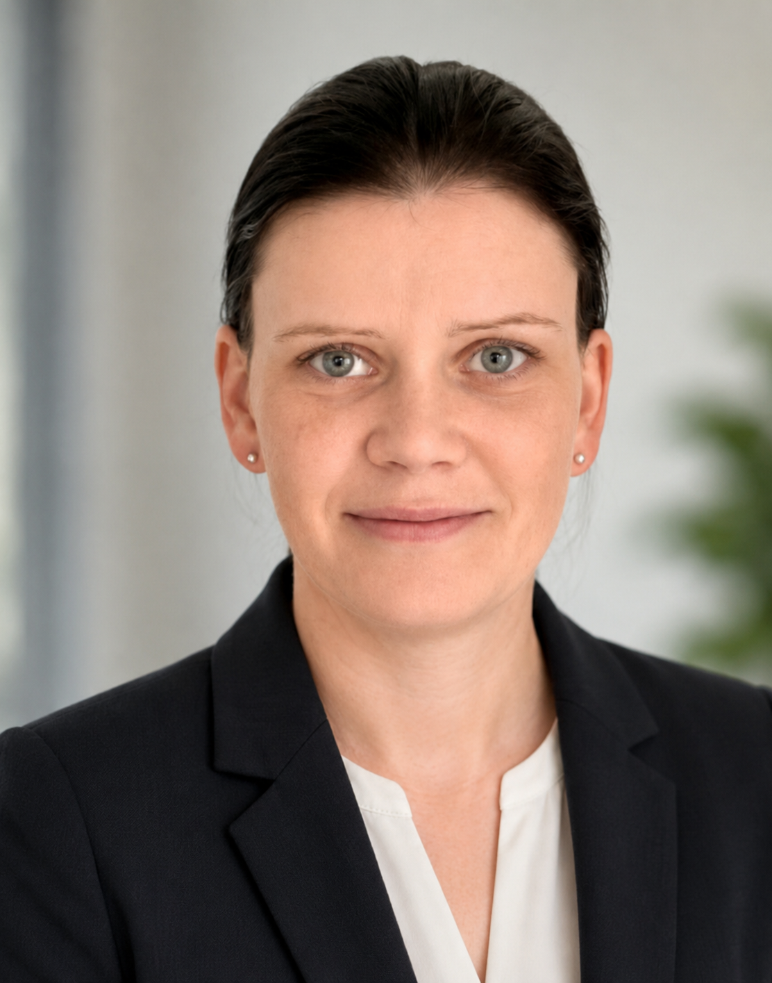 Businesswoman with dark hair, wearing a black blazer and white blouse, smiling in an indoor setting.