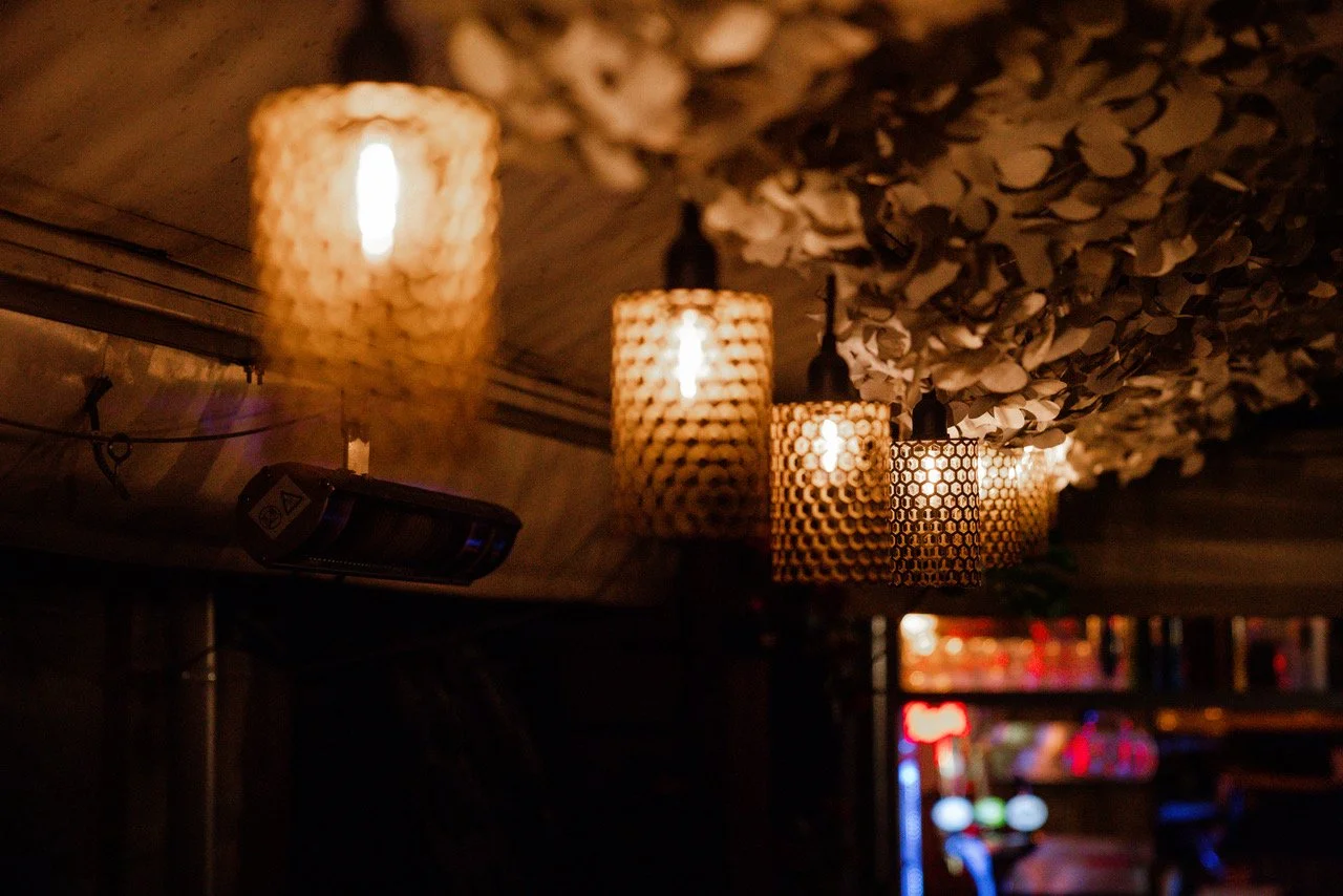 A row of hanging woven pendant lights in a dimly lit interior with a floral ceiling decoration.