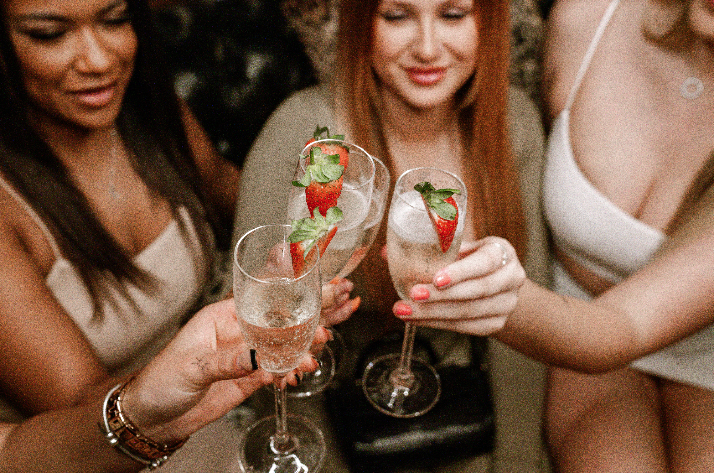 Women celebrating with champagne flutes garnished with strawberries and mint.