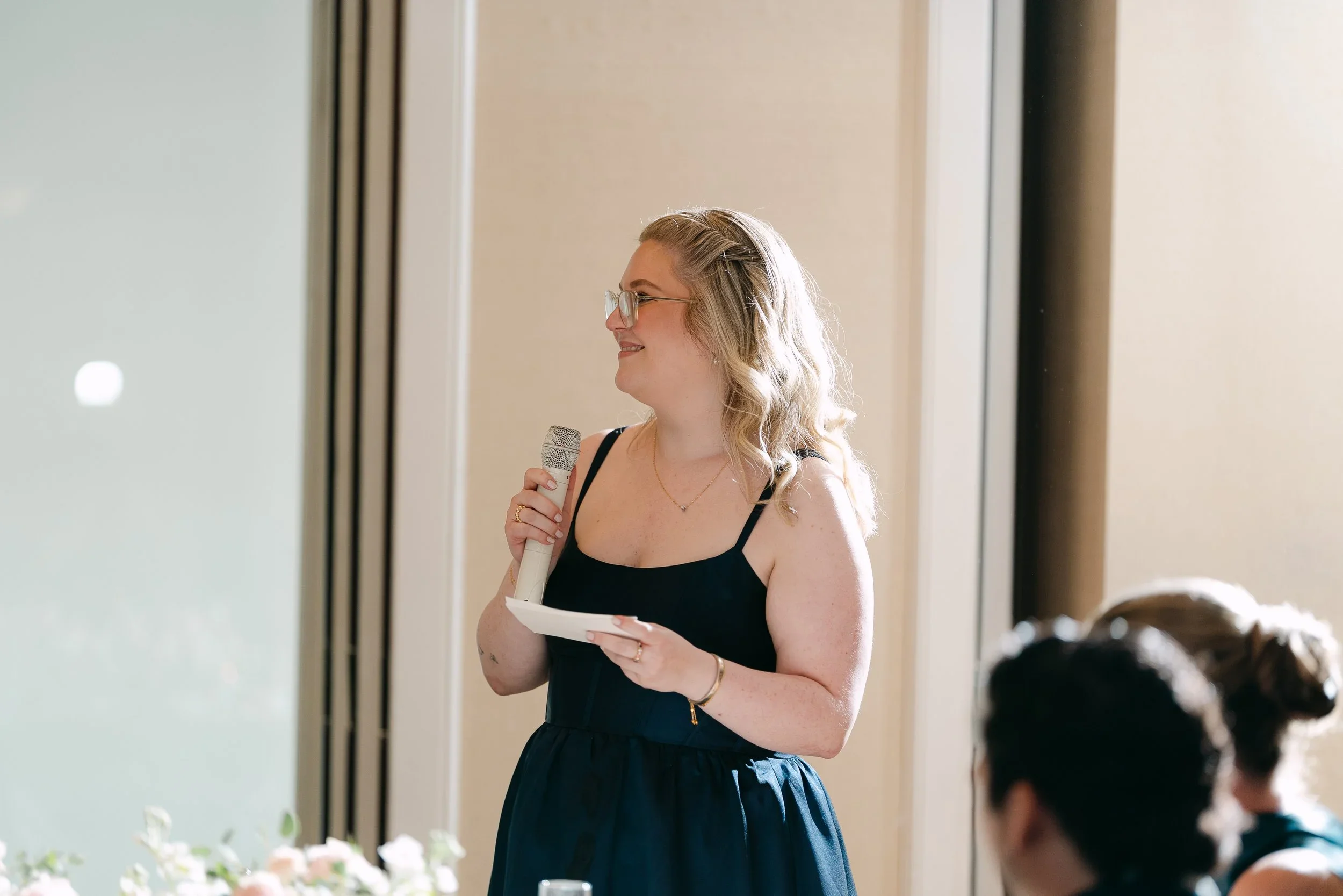 Katie Sullivan holding a microphone and speaking at a wedding reception at Glen Island Harbor Club in New Rochelle, NY