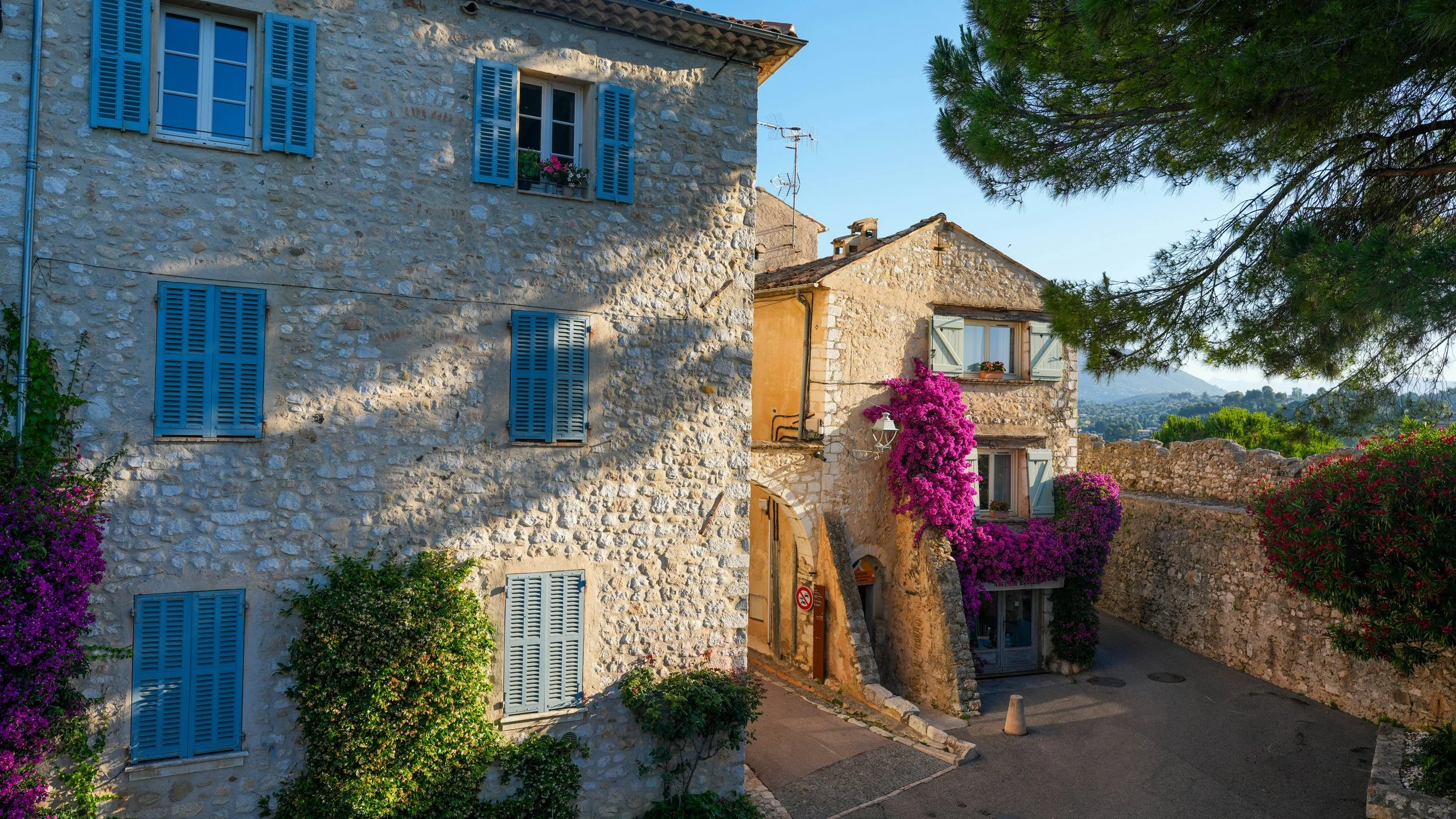 Maisons en pierre avec volets bleus et fleurs roses, arrangement de bâtiments dans un village en Provence