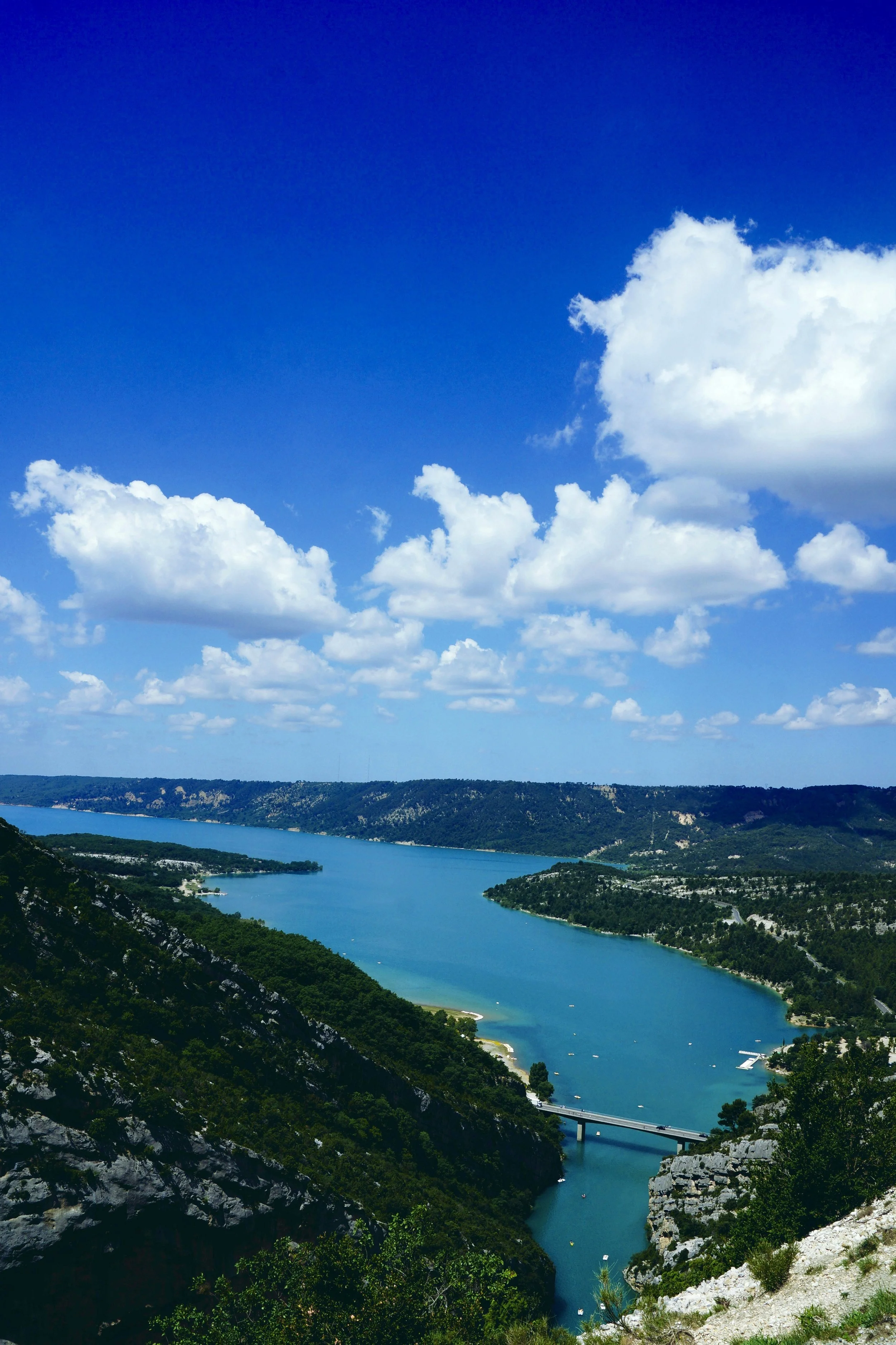 Vue d'une rivière serpentant à travers une vallée verte avec des montagnes en arrière-plan, ciel bleu avec quelques nuages.