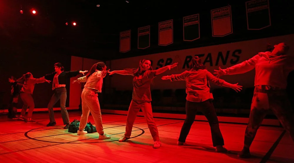 Group of students dancing on a gymnasium floor, illuminated by red lighting.