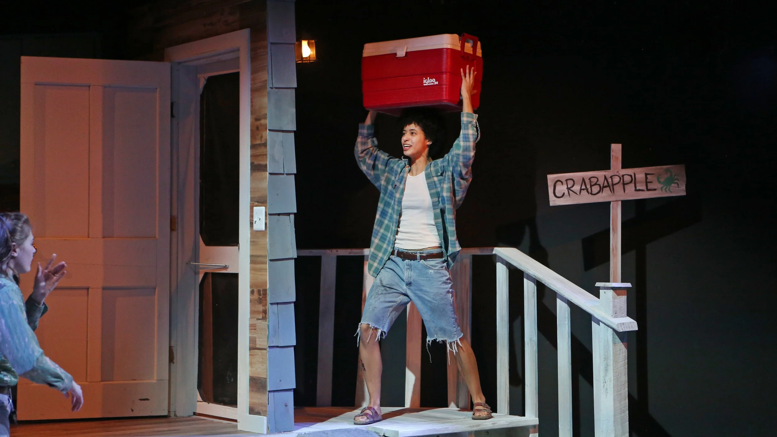 A person holding a red Cooler over their head on a stage with a sign that says "Crabapple" and a small crab illustration. Another person is clapping in the foreground.