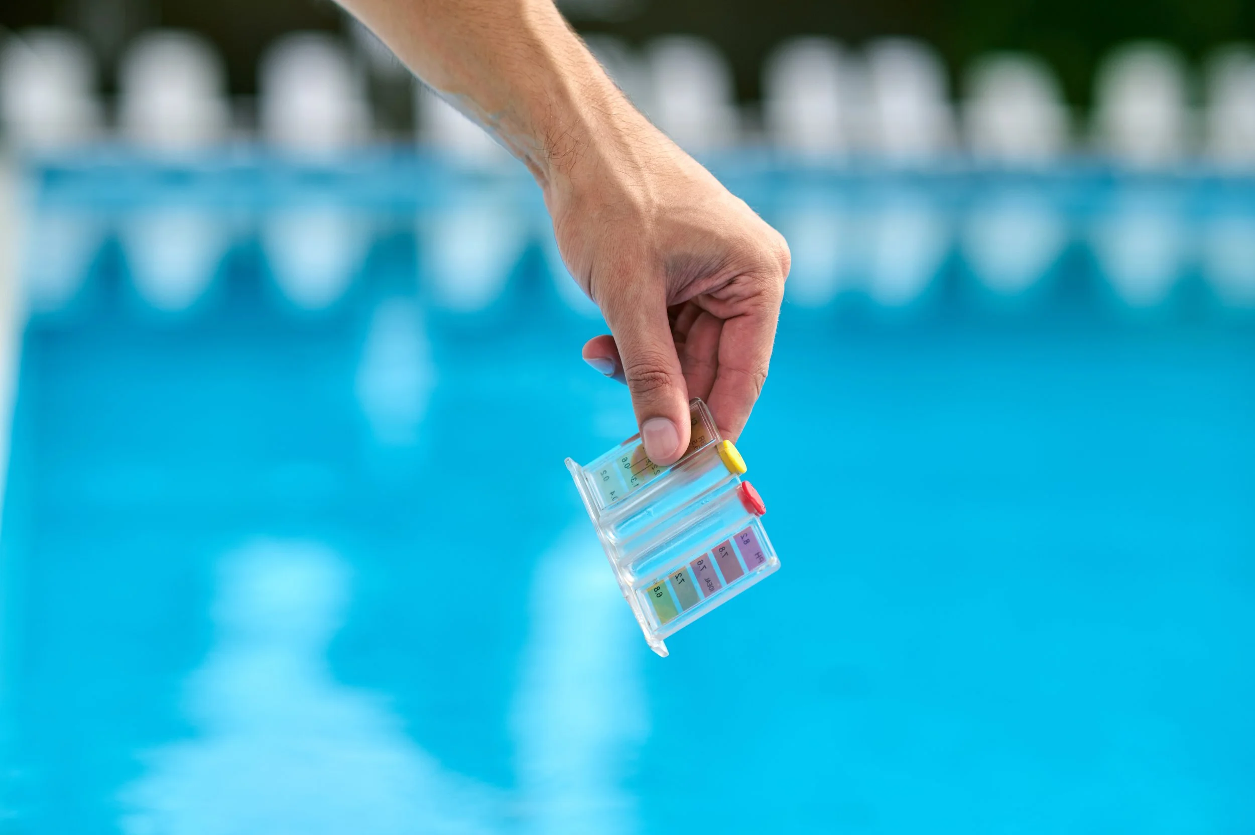 AB Premium Aqua Solutions staff member holding a small laboratory vial over a swimming pool, with a test strip color chart in the background.