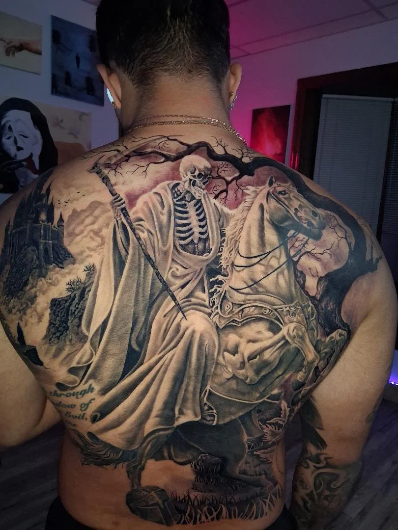 Detailed black and gray tattoo of a skeleton riding a horse, with a background of mountains and a spooky tree with bare branches.