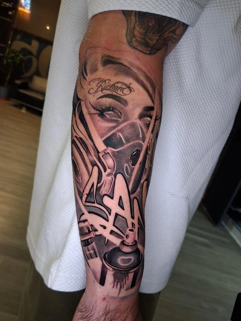 Tattoo of a woman's face with eyeliner and an eyebrow, wearing a respirator mask, with graffiti-style text reading 'SAS' and a spray paint can.