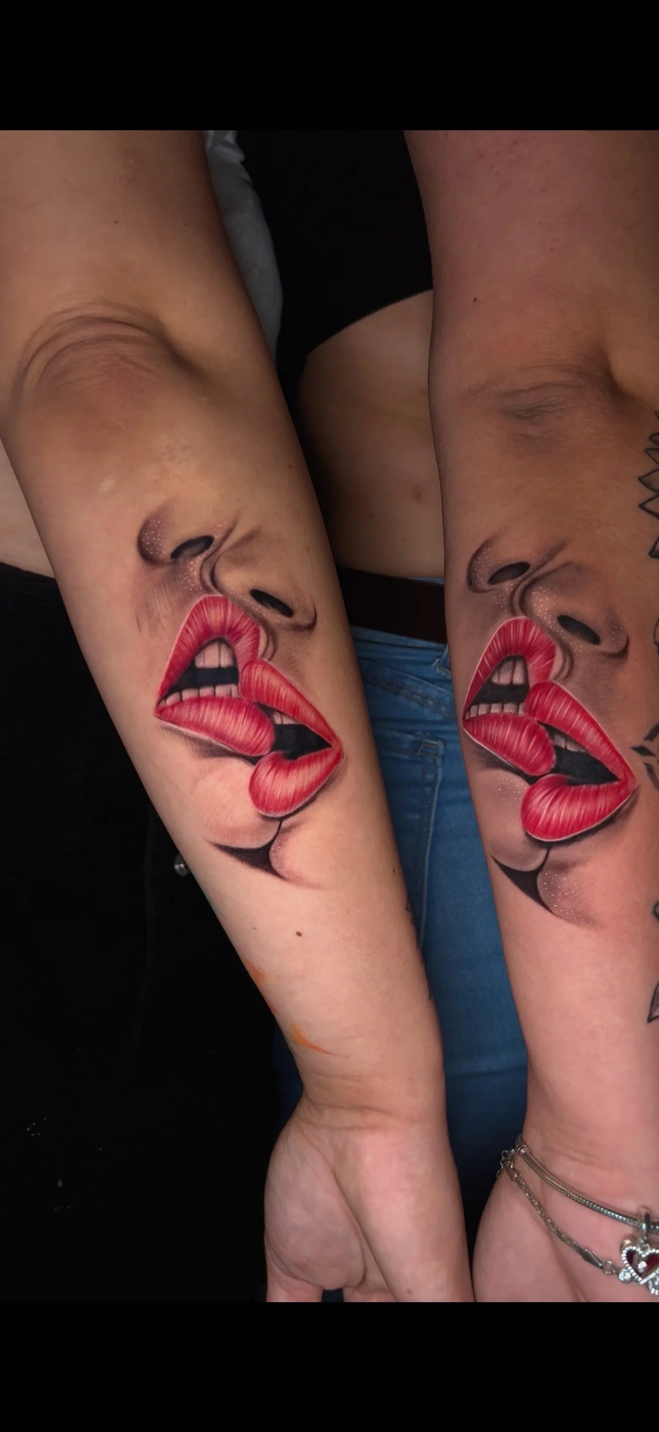 Tattoo of a woman's face with red lipstick, lips parted, on two people's arms.