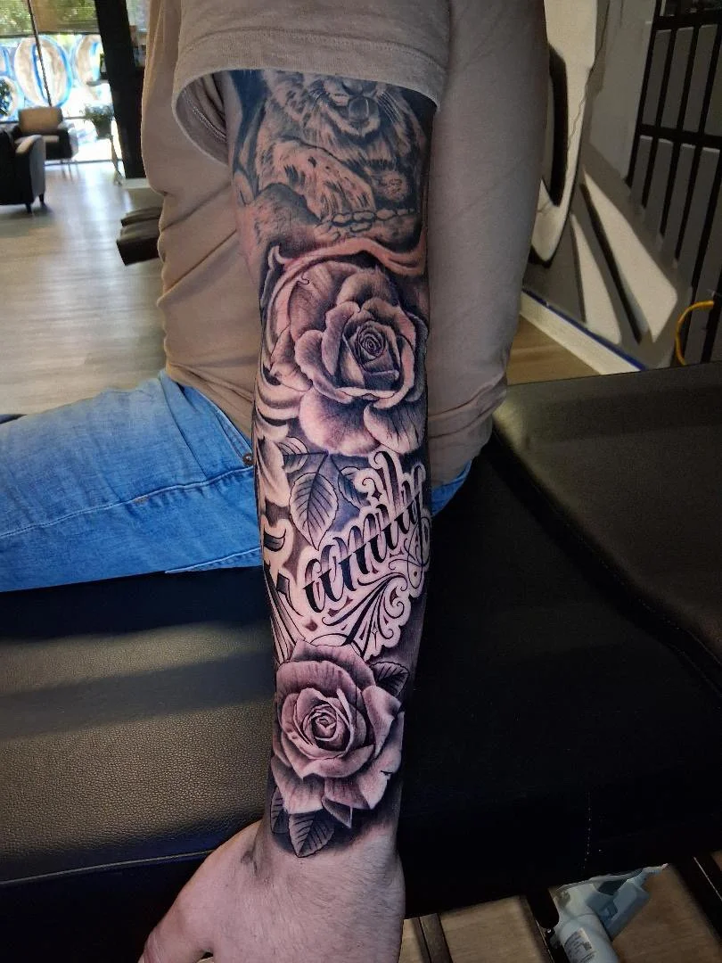 A person's arm with a tattoo of roses and script writing.