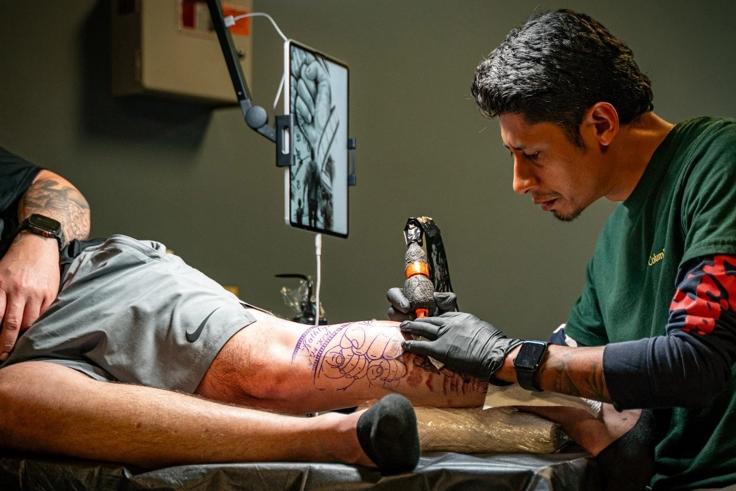 Tattoo artist tattooing a client's leg with a design in a tattoo shop.