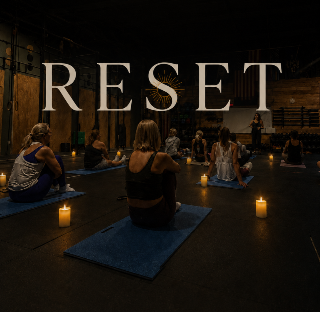 People participating in a yoga class in a dimly lit studio with candles, wooden walls, and fitness equipment, with a instructor leading the session.