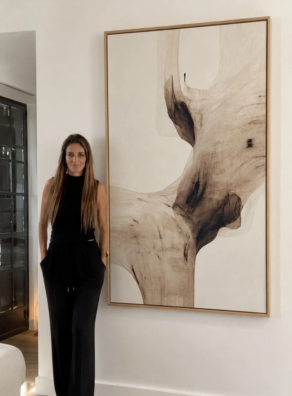 Woman with long hair in black sleeveless top and black pants standing beside a large abstract wood art piece on a white wall