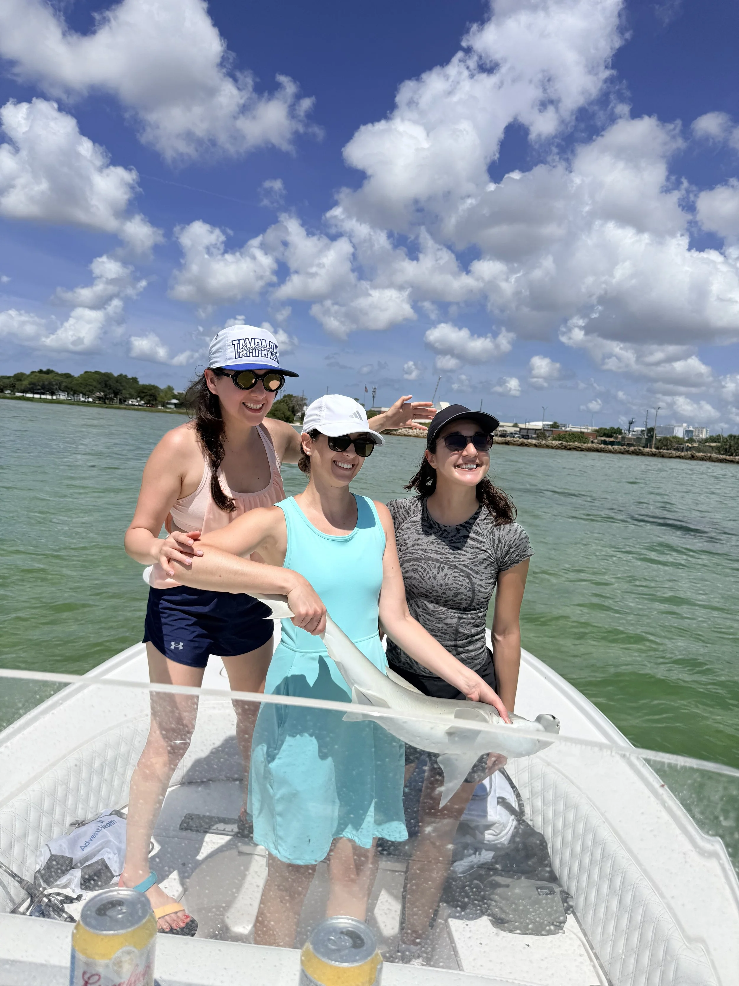 Three women are on a boat in a body of water under a partly cloudy sky, smiling and enjoying the day.