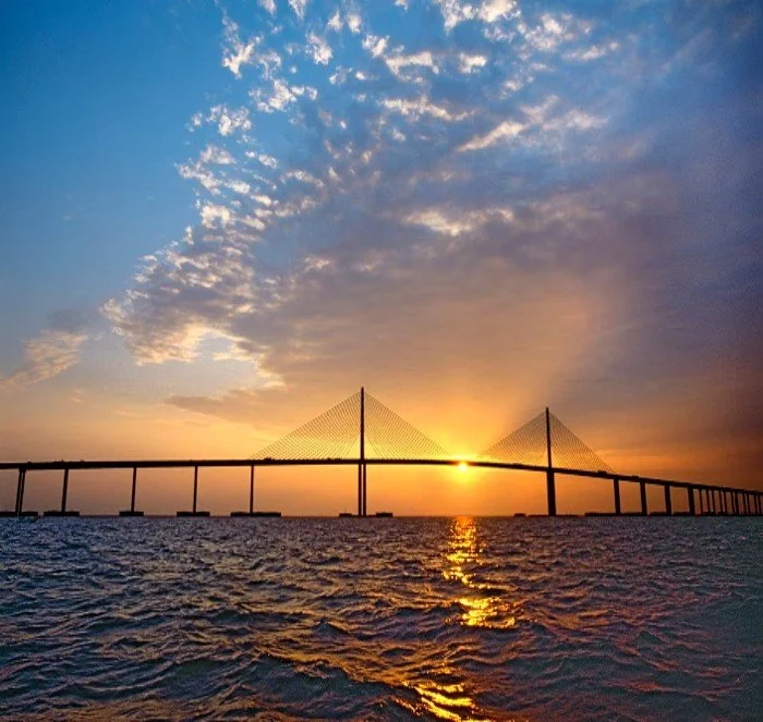 A bridge at sunset over the water with a partly cloudy sky.
