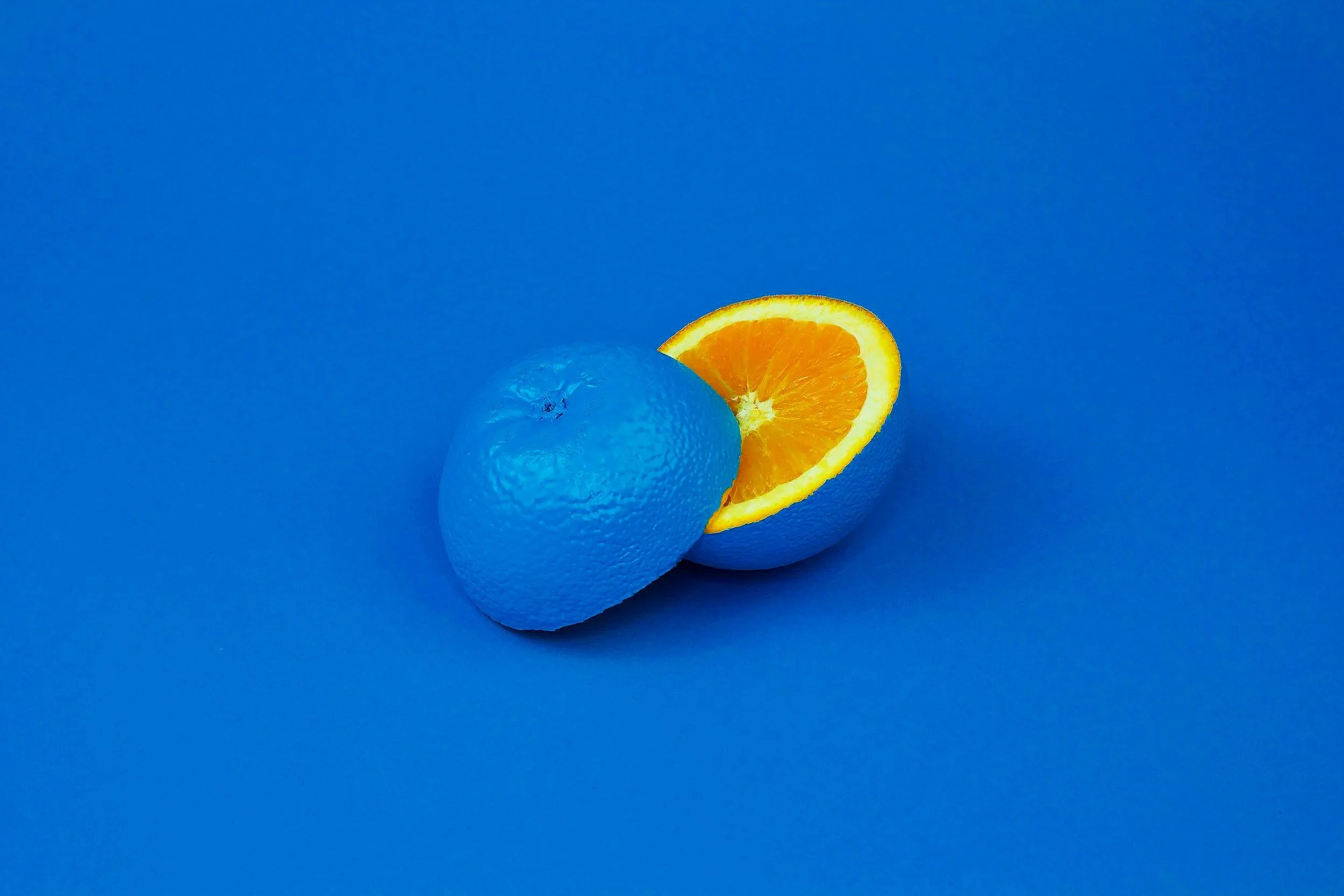 A slice of orange resting against a whole blue textured sphere, with a blue background.