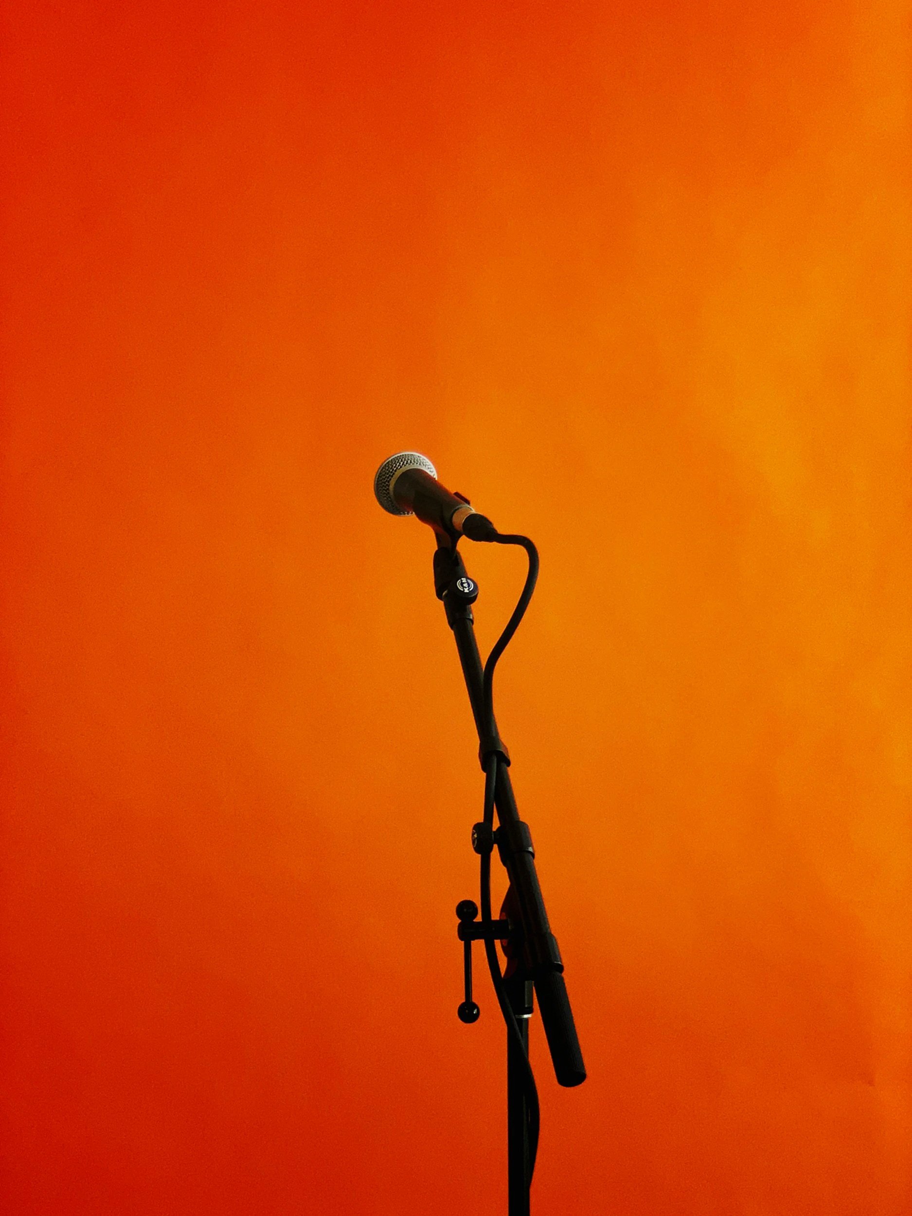 A microphone on a stand against an orange background.