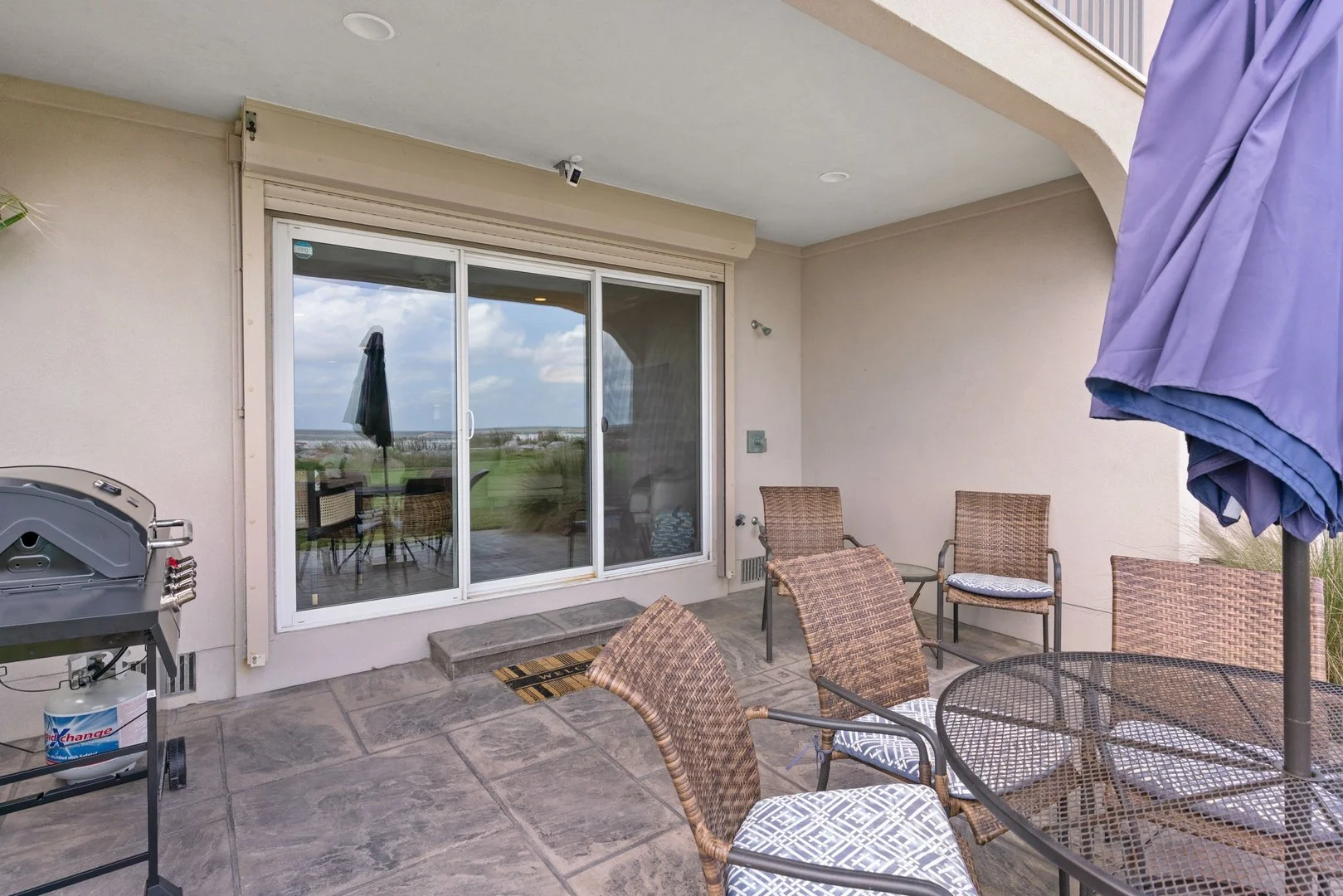 Beach side patio featuring a gas grill, seating for 8, sliding door, and beach gear.