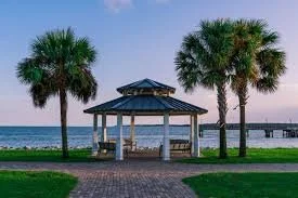 A gazebo near the pier in the village wiht two palm trees on either side and a paved walkway in front.