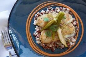 A bowl of rice topped with plantains, a green chili pepper, and garnished with basil leaves, served on a blue plate.
