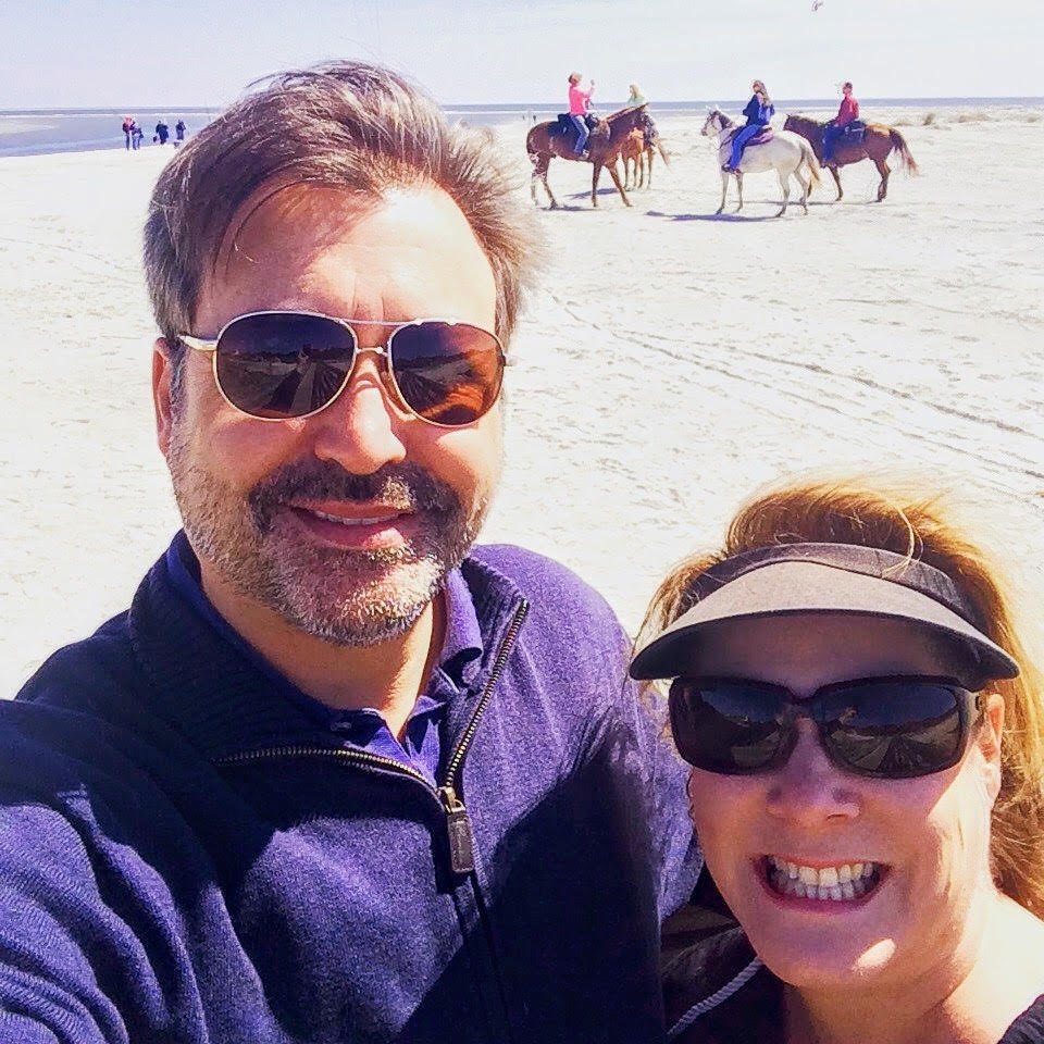 The owners on a beach, with a group of people riding horses in the background.