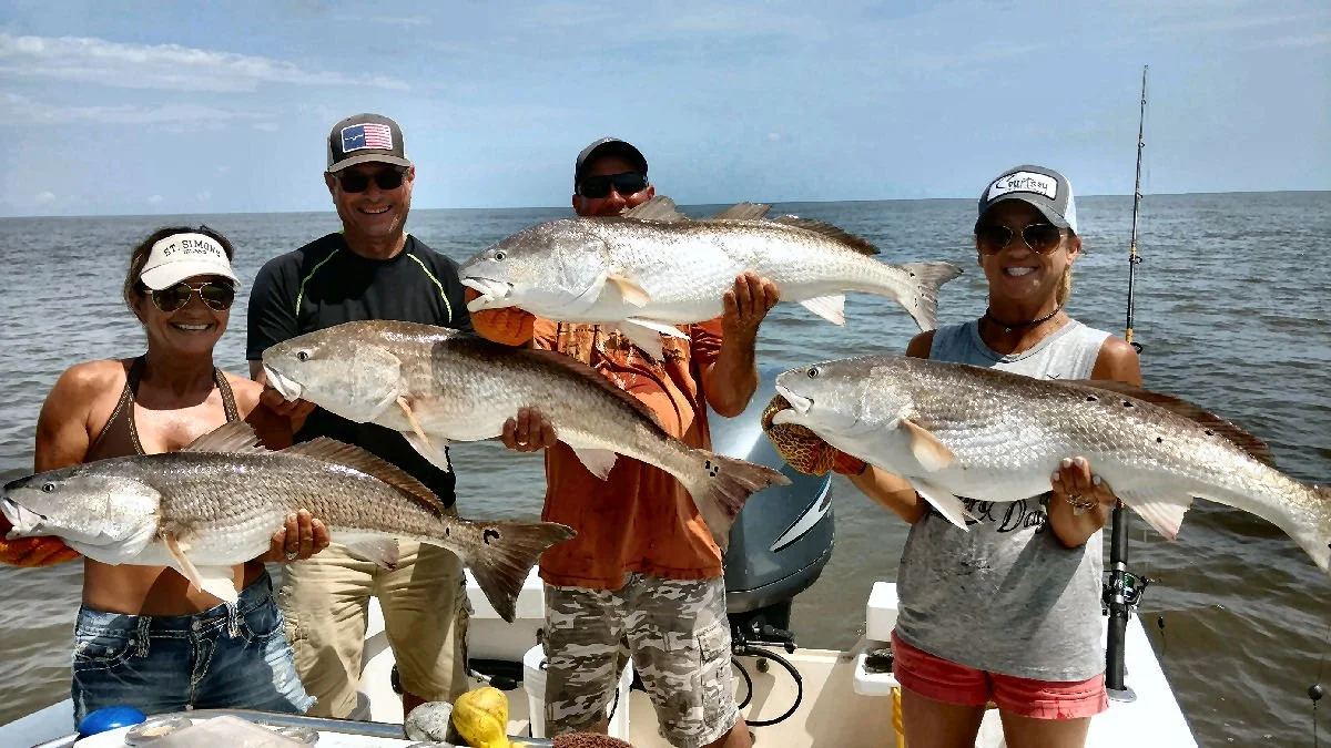 Group of five people holding large fish on a boat at sea, smiling and wearing sunglasses and hats.