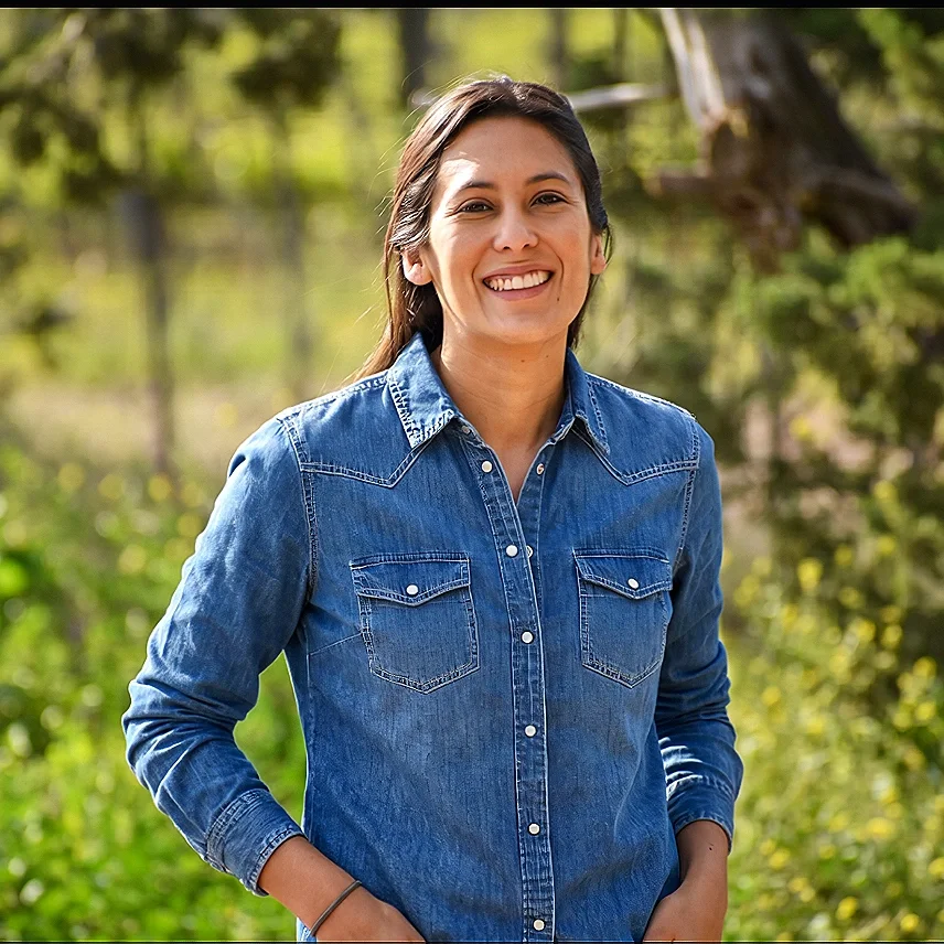 Mujer profesional sonriendo en un entorno natural, especificamente rodeada de viñedos en Mendoza.