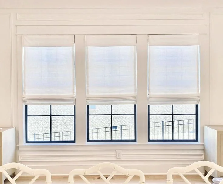 Three large windows with white blinds in a bright, white room.