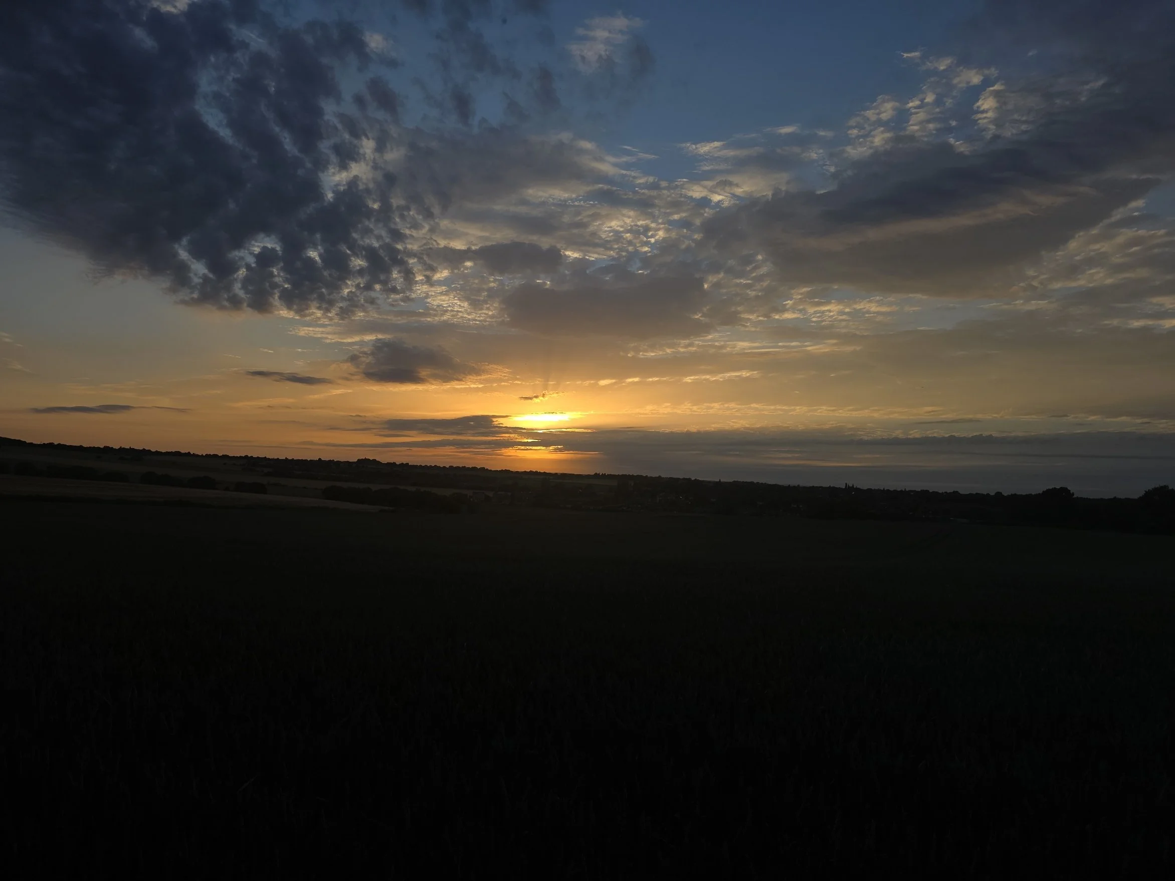 Sunset over the horizon with clouds in the sky and a dark landscape below.