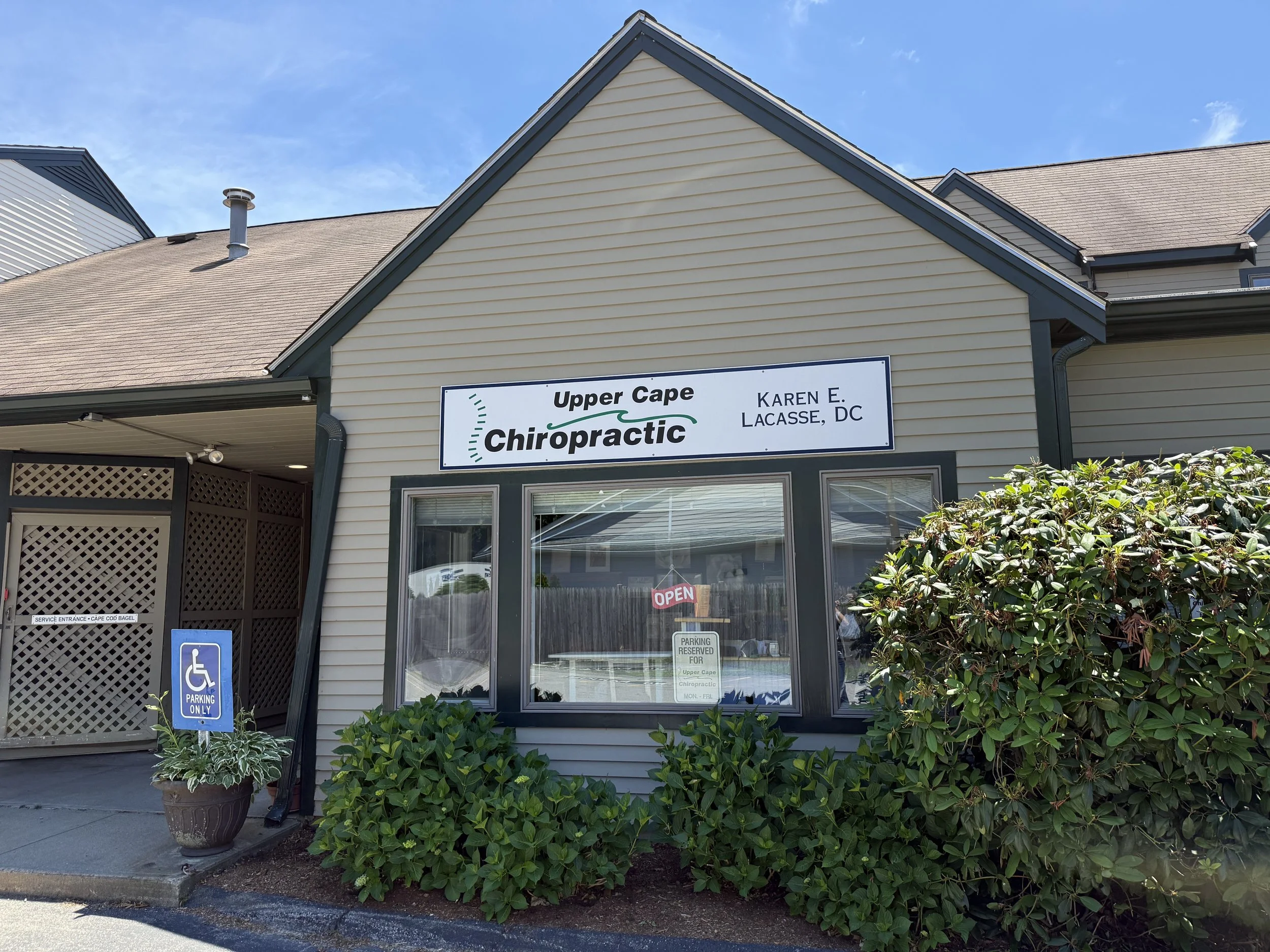 Exterior view of a building with a sign reading 'Upper Cape Chiropractic' and an additional sign indicating parking for disabled persons. Potted plants are in front of the building, and there is an