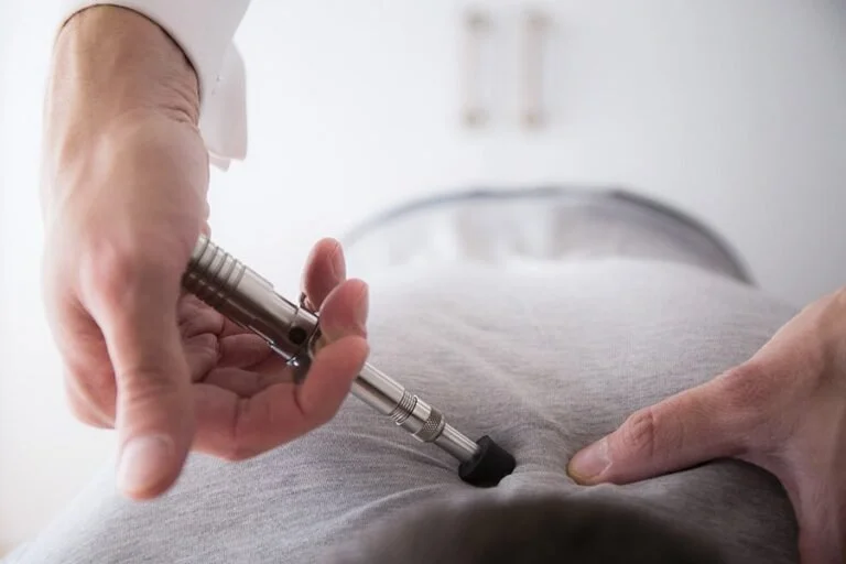 Person receiving chiropractic treatment with a handheld instrument on their lower back.