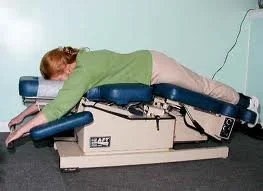 Person lying face down on a chiropractic adjustment table with an electronic device attached, receiving treatment.