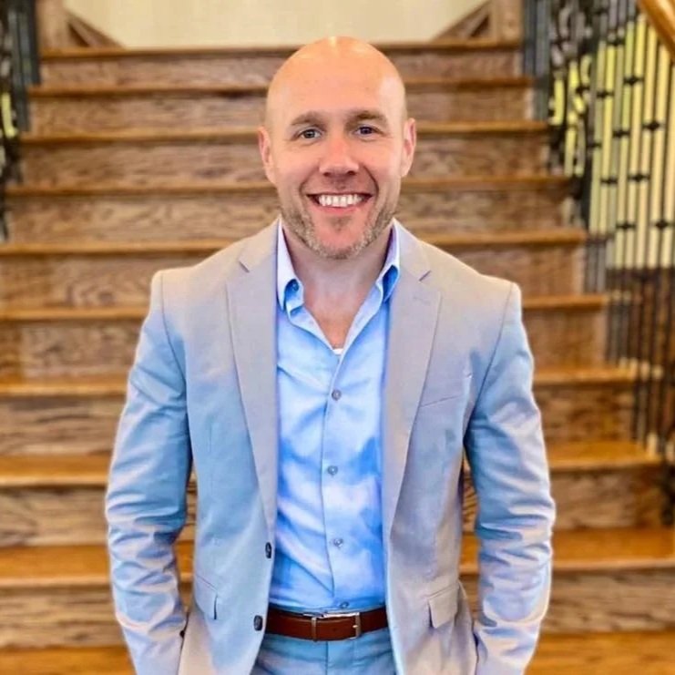David Beard, Director of Policy & Government Affairs   The Children & Nature Network, Man in gray suit and blue shirt smiling, standing in front of wooden staircase.