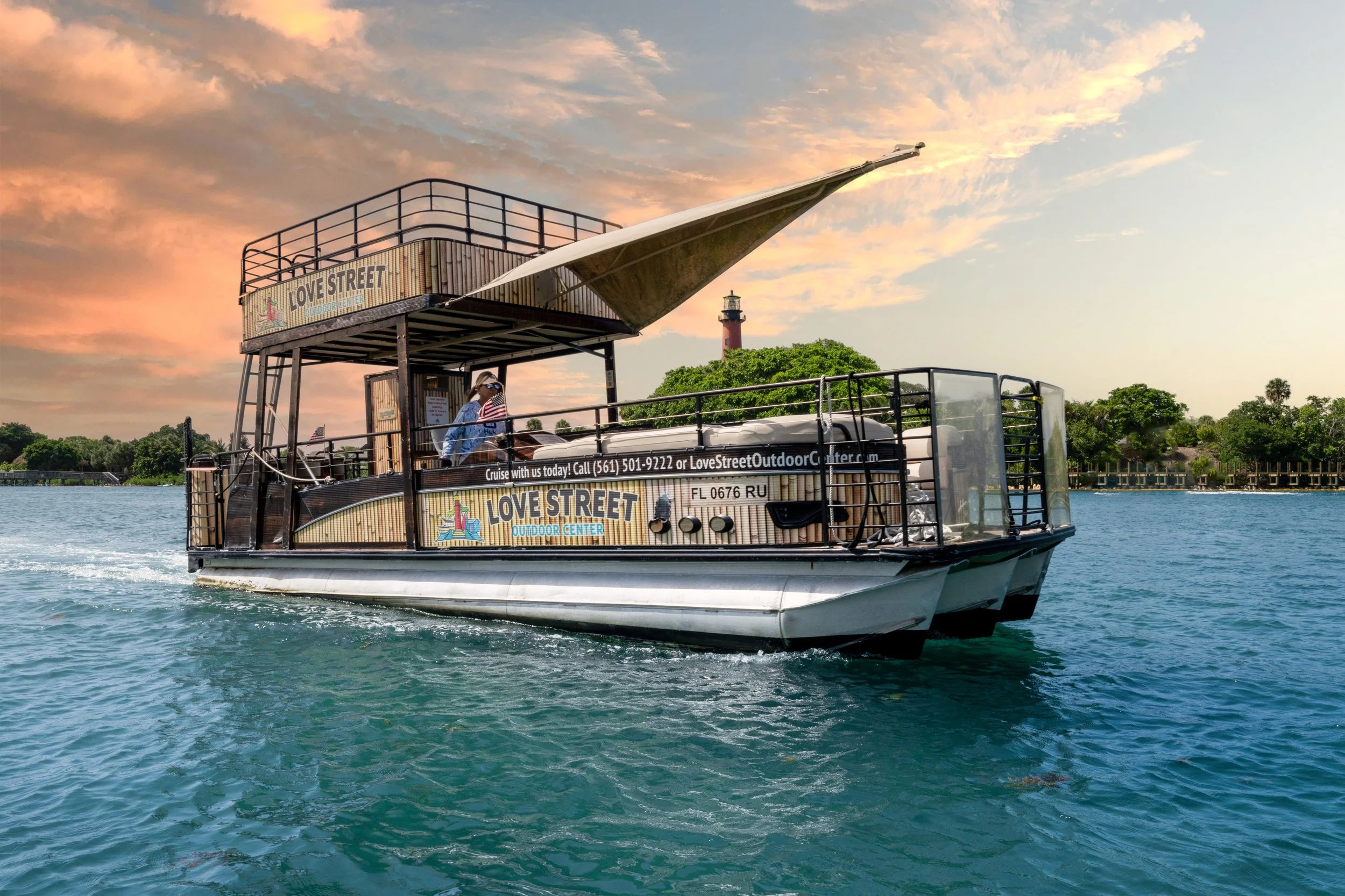 A boat labeled 'Love Street Outdoor Center' is on the water during sunset, with a lighthouse and trees in the background.