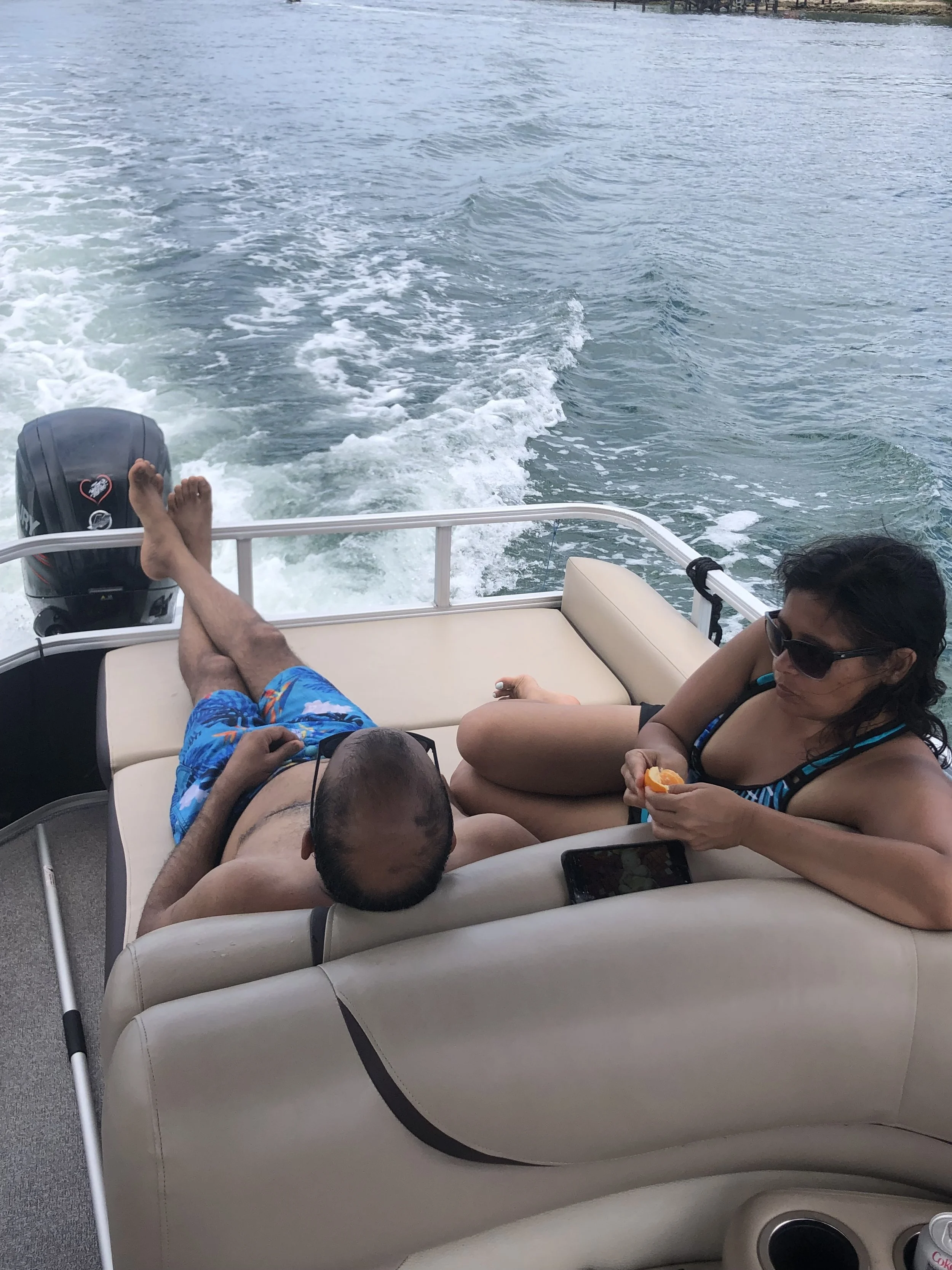 People relaxing on a boat, with the person's legs stretched out and an outboard motor visible on the back, as the boat moves through water with small waves.