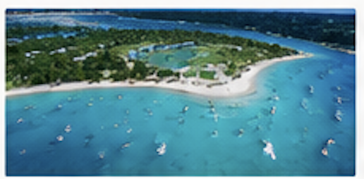 Aerial view of a tropical island with white sandy beaches, surrounded by clear blue water with boats docked near the shore.