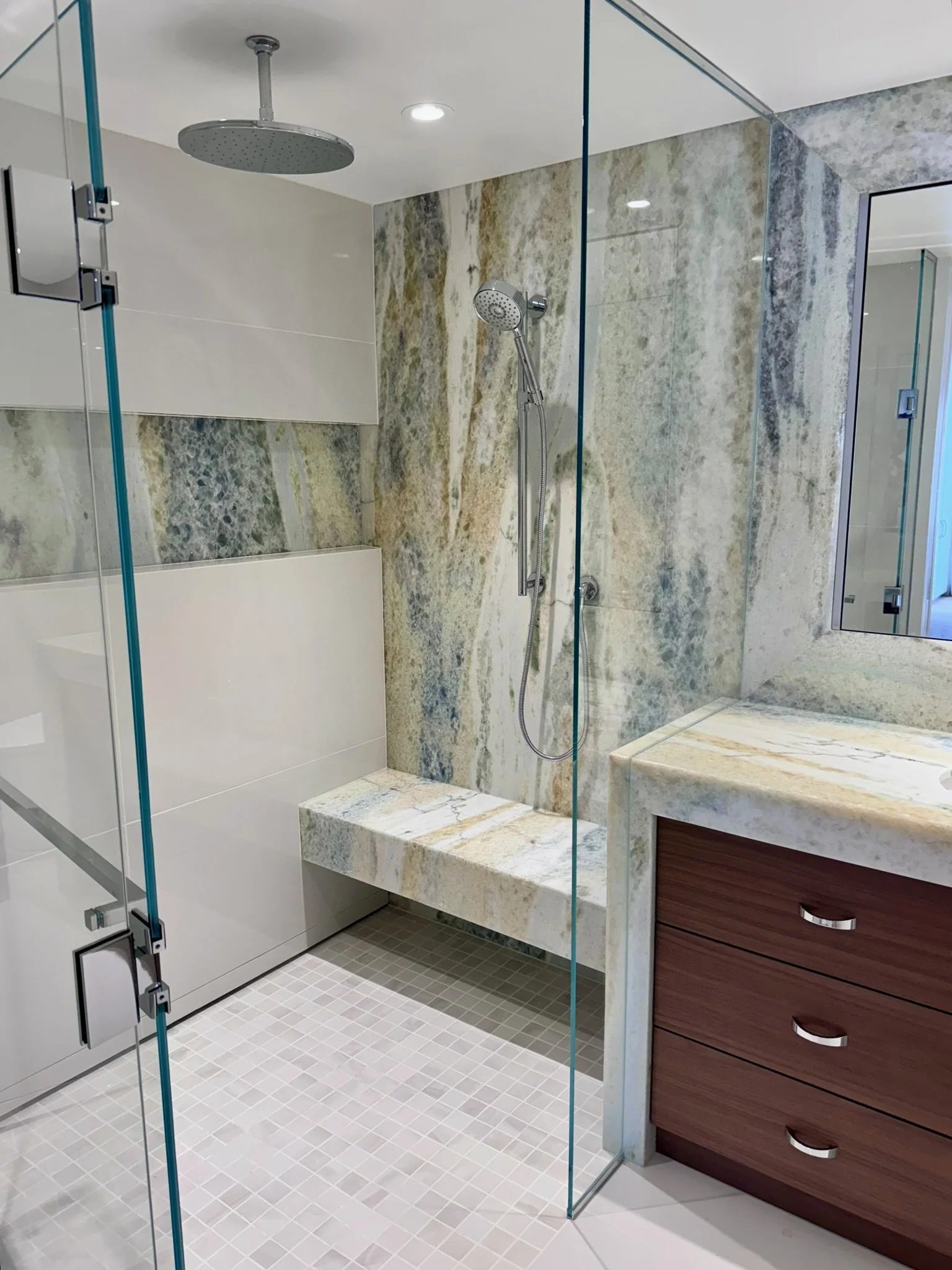 Modern bathroom with a glass shower enclosure, shower head, a marble ledge, and a wooden vanity with drawers.