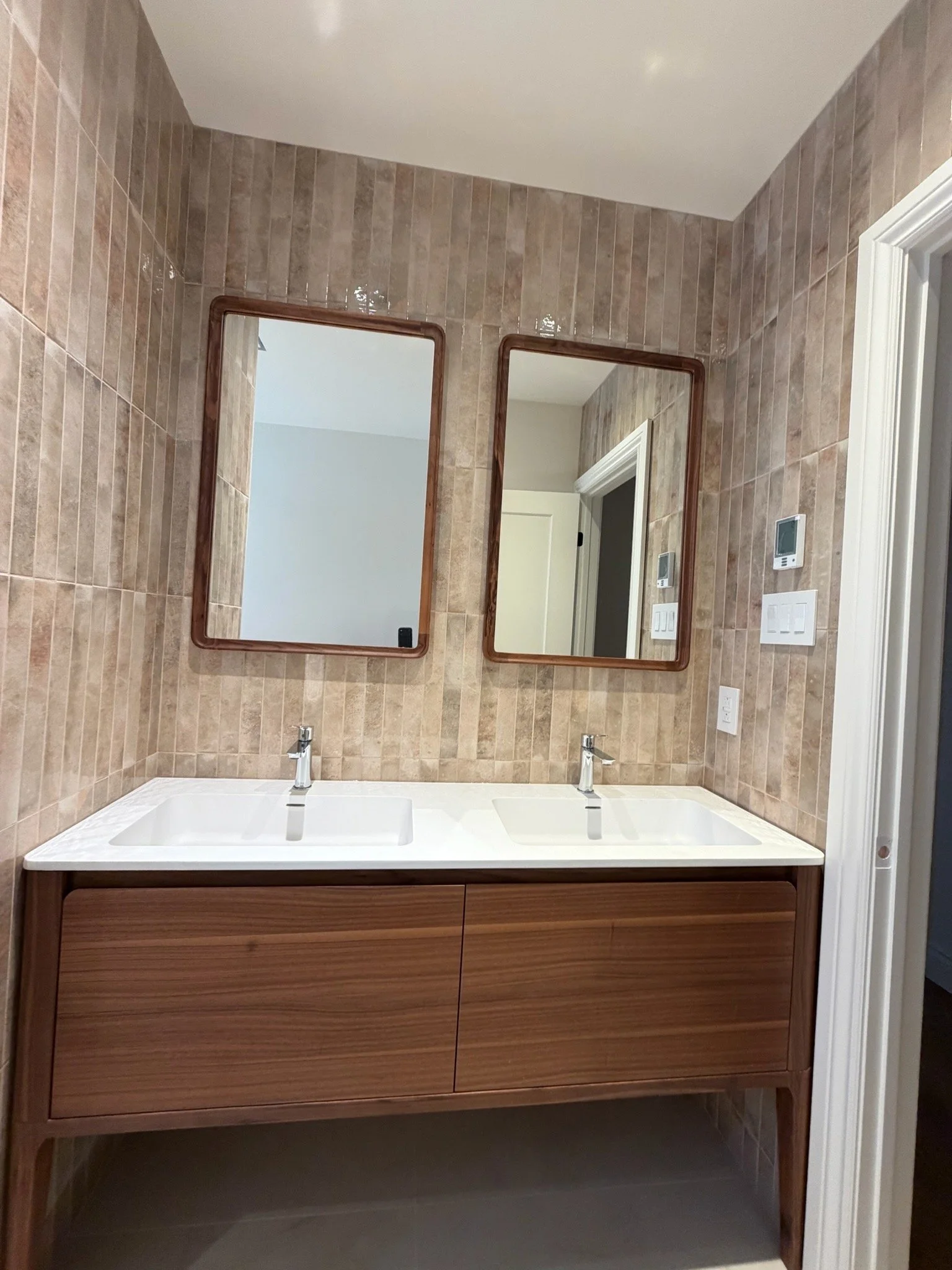 A modern bathroom vanity with a double sink, wooden cabinet, and two mirrors on a tiled wall.