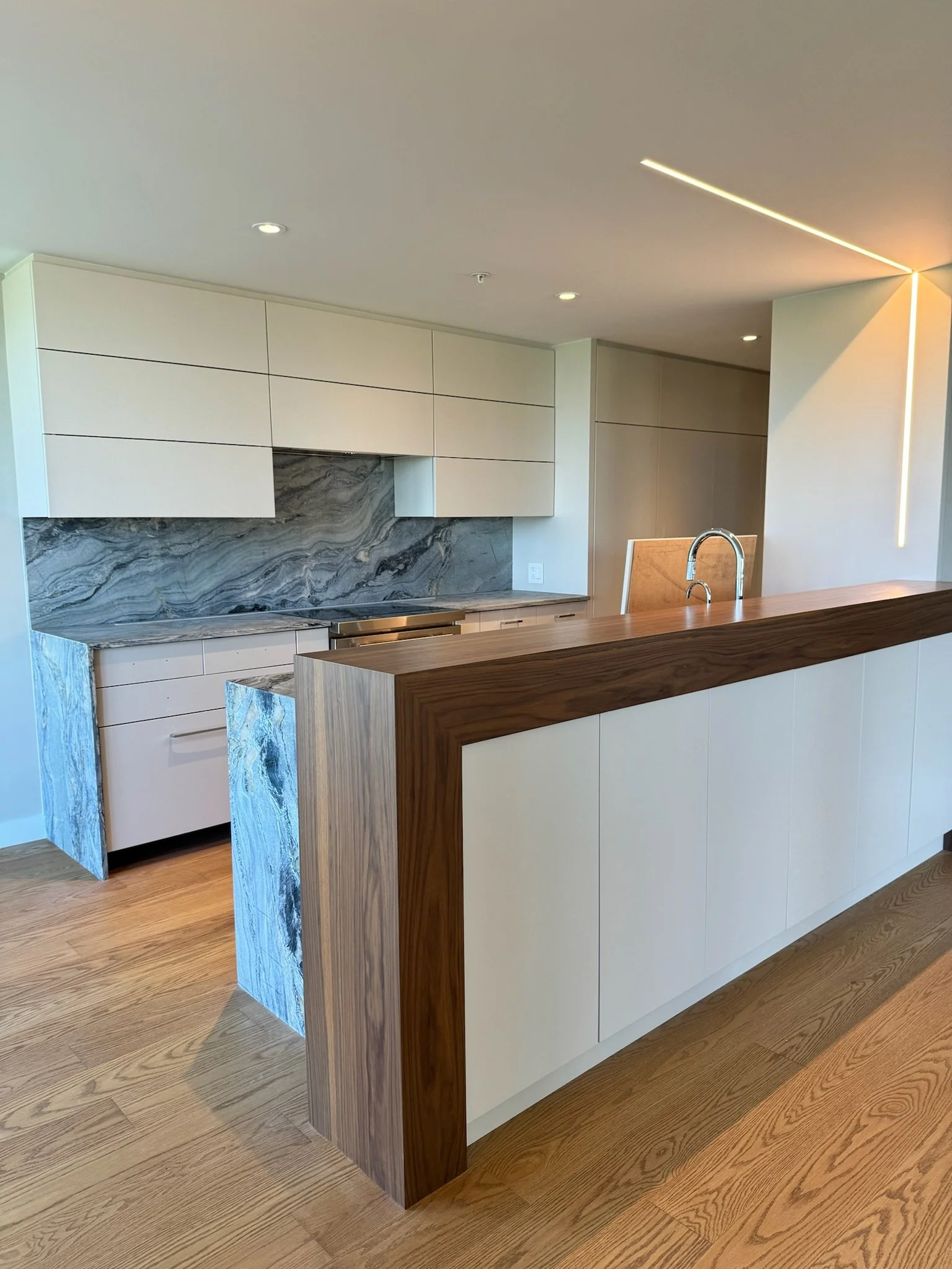 Modern kitchen with white cabinets, a marble backsplash, a wooden island with a built-in sink, and hardwood floors.